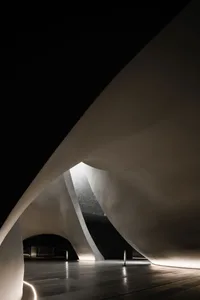 Interior space with concrete walls and floor, featuring curved architectural elements and illuminated by light from above.