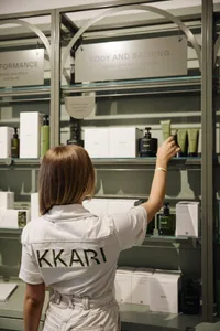 A woman in a white shirt is arranging bottles on a glass shelf in a retail setting.