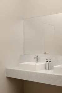 A modern restroom features a white mosaic-tile backsplash with steel trim, a sleek white sink, and silver soap dispensers. Th