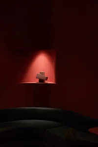 極簡室內空間，紅色置物架上擺放混凝土塊，旁有黑色弧形沙發