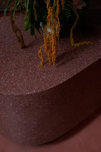 A sleek, modern table made of red terrazzo with a smooth, rounded surface, featuring a plant with yellow flowers in a white v