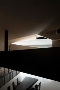 A modern minimalist dining room with concrete floors and walls, featuring black furniture and a large skylight.
