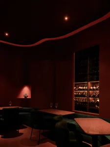 A dimly lit modern restaurant bar featuring a rustic, industrial ambiance with terrazzo tables and wine bottles on display.