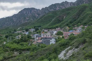 A residential landscape with houses nestled among lush green hills and mountains in the background.