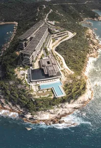 A modern resort built into a hillside, featuring concrete structures, glass storefronts, and a green roof adorned with trees.