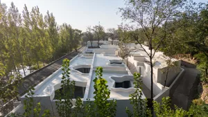 A modern white concrete residence with curved rooftops surrounded by trees and greenery.