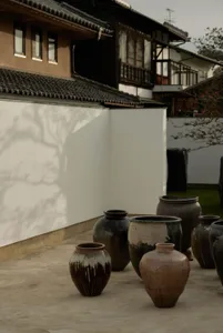 Several ceramic pots and vases are placed outside a traditional-looking building with a tiled roof.