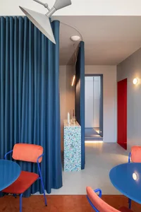 Modern industrial office space with concrete walls, glass partitions, blue tiles, and L-shaped furniture.