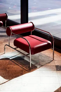 A modern red leather accent chair with a metal frame, placed in front of a large window.