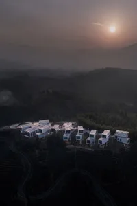 Aerial view of modern residential buildings on a hilltop with terraced fields and distant mountains.
