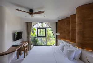 A minimalist bedroom featuring a white bed with a wicker headboard and wooden desk area.
