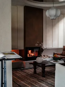 A modern living room with a concrete fireplace, wood accents, and a striped rug.