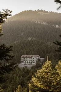 A stone hotel building nestled in a forested mountain landscape.