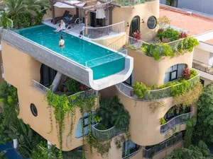 Scenic view of a modern residential building exterior with a large infinity pool on the roof, surrounded by greenery and arch