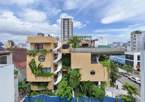 A modern building with concrete and glass exterior features greenery and balconies.
