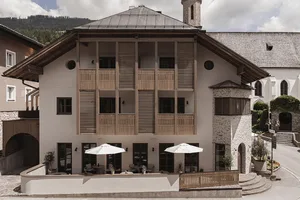 A modern hotel with stone and wooden exterior, featuring exterior balconies and a stone staircase.
