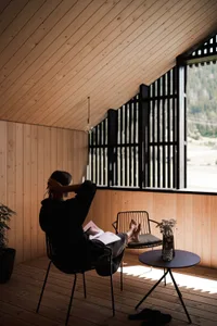 A cozy wooden retreat with a person relaxing in a chair, looking out of a window with a view of nature.