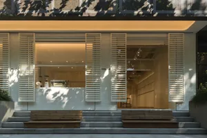 Modern coffee shop with white wooden shutters and glass door, featuring concrete flooring and minimalist design.