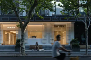 A modern street scene featuring a shop with warm lighting, a person sitting, a dog lying down, and a cyclist passing by.