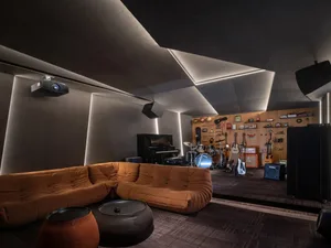 A spacious industrial music studio featuring a plush sofa, a variety of musical instruments, and acoustic foam panels on the 