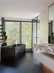 Modern bathroom with marble countertop, glass shower enclosure, and black metal bathtub.