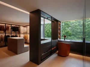 Modern closet with wooden and glass walls featuring organized clothing and a comfortable sitting area.