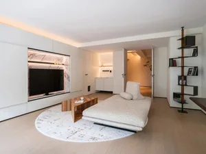 A modern minimalist living room featuring wooden furniture, a round rug, and a flat-screen TV.