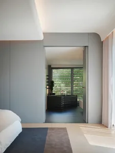 A minimalist bedroom with grey walls, a black bathtub, and large windows with vertical blinds.