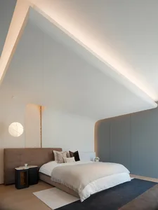 A modern minimalist bedroom featuring a white bed with a fabric headboard, a gray carpet, and a sleek, contemporary design.