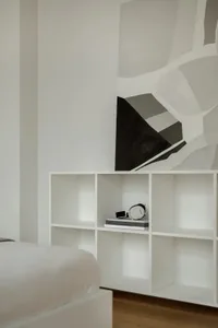 A minimalist bedroom with a white bookshelf on a wooden floor.