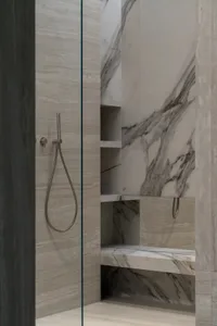A modern bathroom with a marble shower niche and shower head mounted to the wall.