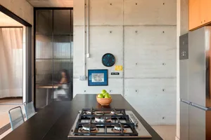 A modern, industrial kitchen with concrete walls, a black countertop, a stainless steel stove, and a bowl of green apples.