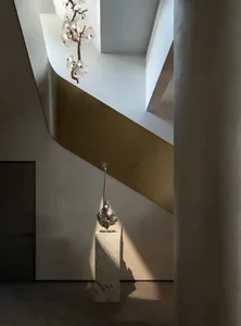 A metallic art object displayed on a white pedestal in a modern interior space.