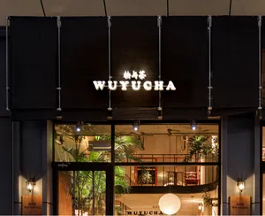 Modern storefront with glass facade, lights, and greenery inside.