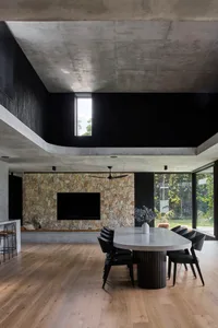Modern minimalist dining room with a stone wall, a large table, and black chairs, featuring a high ceiling and large windows.