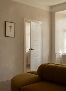 A minimalist living room featuring a comfortable, plush brown sofa with a sofa table sitting behind it. The room is illuminat