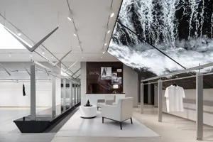 A minimalist retail store with a large black and white ocean waves mural, white furniture, and a sailboat model.