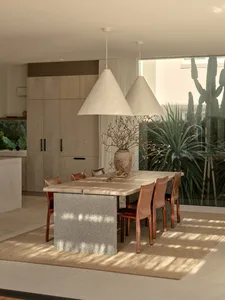 A modern minimalist dining room with a wooden table and leather chairs, featuring a concrete base and hanging pendant lights.