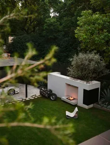 A modern outdoor living space with a concrete fireplace and greenery.
