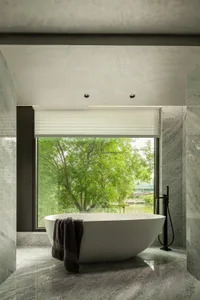 A modern bathroom features a freestanding tub surrounded by marble walls and floors, with a window overlooking lush greenery 