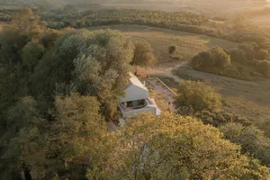 A minimalist house made of white concrete, surrounded by green trees and fields.