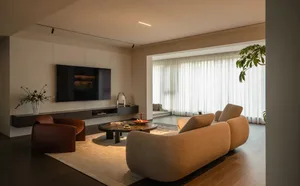 A minimalist living room featuring wooden flooring, fabric furniture, and glass elements.