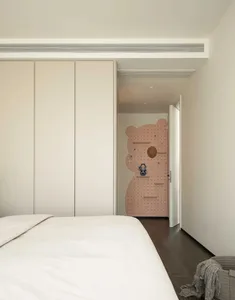 A minimalist bedroom featuring a white bed with a modern design, surrounded by white closet doors and a pink pegboard wall fe