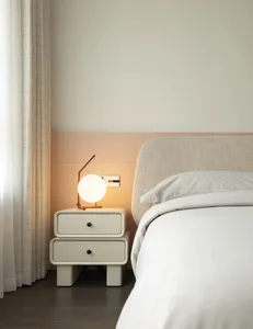 Minimalist modern bedroom with fabric bed, white bedding, and white nightstand with a round lamp.
