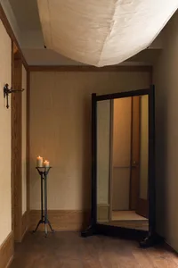 A minimalist bedroom with wooden floors, a candle holder with two lit candles, and a large mirror reflecting a door.