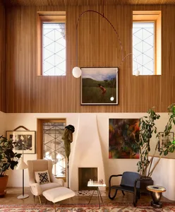A minimalist living room featuring a teak-paneled wall, a black armchair, and a white armchair with an ottoman, along with va