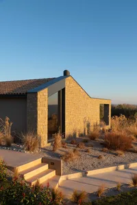 A modern residential house with a stone exterior, featuring large windows and a flat roof.