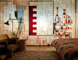 A minimalist bedroom with a bed covered in a patterned blanket, a sofa, and potted plants.