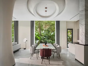 Modern dining room with a marble table surrounded by fabric chairs, featuring a large garden view.