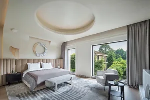 A modern, minimalist bedroom with a large bed, window, and white decor.